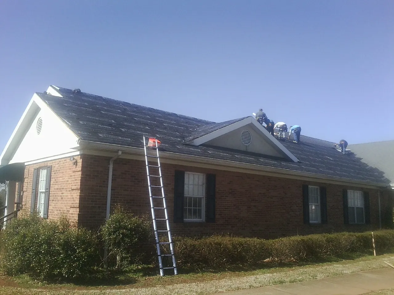 Crew tearing shingles off a brick ranch roof with a ladder set — Metal Roof Repair work by our crew in Flag Pond