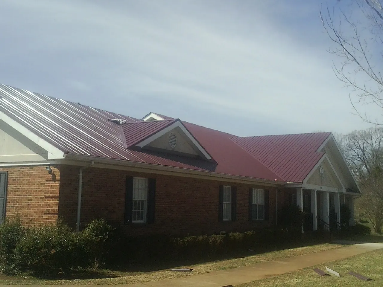 Red metal roof with gabled entries on a long brick building, from a Hail Damage Roof Repair job in Flag Pond