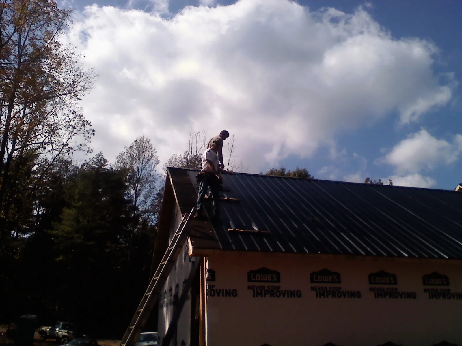 Roofer fastening dark metal panels high against a cloudy sky, from a Roof Inspection job in Flag Pond