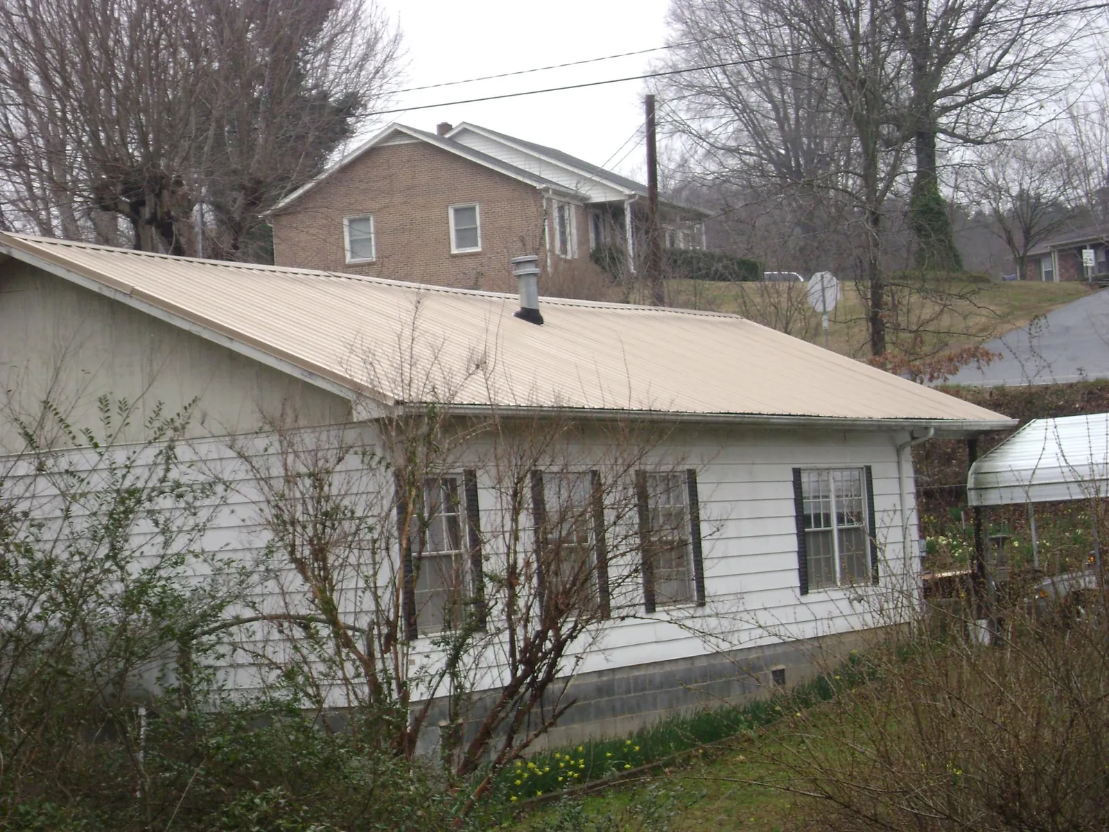 Tan metal roof on a white sided house set into a hillside — Commercial Roofing by Roofing Brothers in Flag Pond