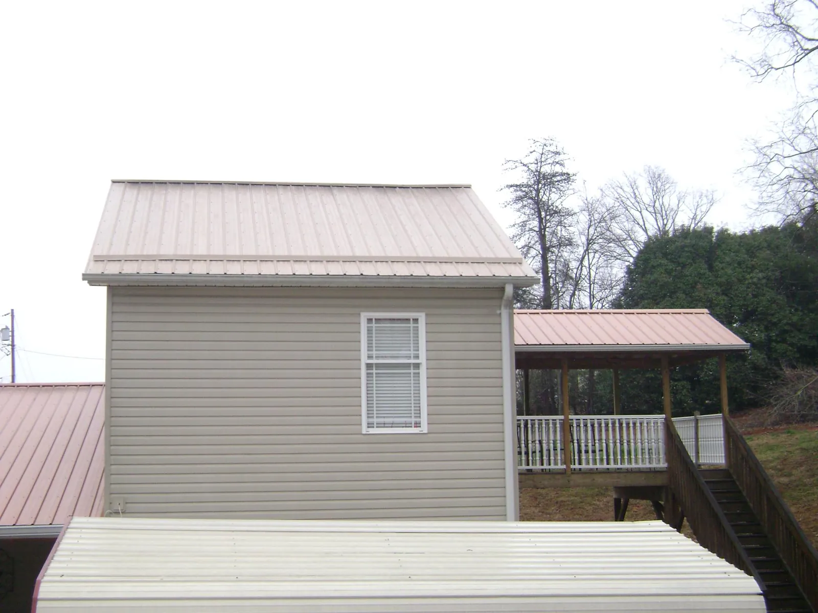 Tan metal roofs on a two story addition and attached porch, from a Roof Replacement job in Flag Pond